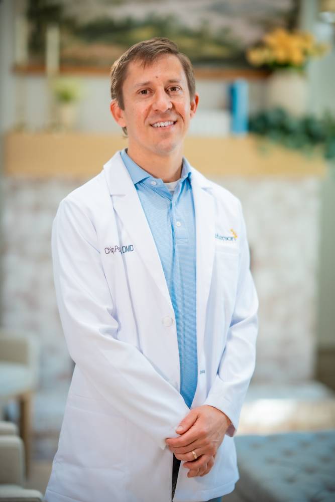 Dr. Chip Patterson, DMD, smiling in a white lab coat over a light blue collared shirt at Patterson Family Smiles in Clayton, GA 